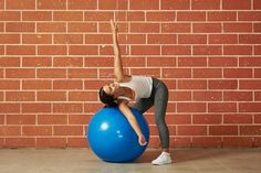 a woman is doing exercises on an exercise ball in front of a red brick wall