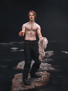 a man with no shirt standing on rocks in the water