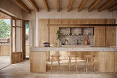 a kitchen with wooden cabinets and marble counter tops, along with two stools in front of the bar