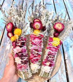 a basket filled with dried flowers sitting on top of a wooden table next to a person's hand