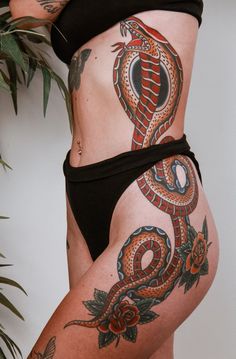 a woman with a snake tattoo on her stomach and lower body is standing next to a potted plant