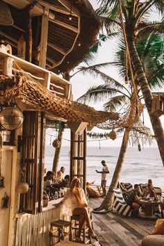 people sitting at tables on the beach with palm trees in the foreground and ocean in the background