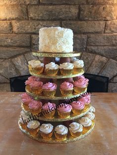 a three tiered cake with cupcakes on the bottom and sides, sitting on a table in front of a fireplace