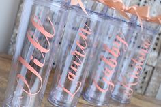 four personalized tumblers are lined up on a wooden table with pink ribbons and bows