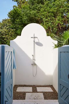 an outdoor shower in the middle of a garden with blue shutters and white walls