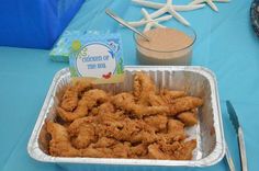 a table topped with a tin pan filled with fried chicken