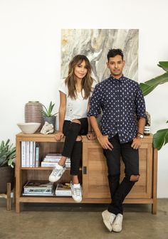 a man and woman sitting on top of a wooden cabinet in front of a painting