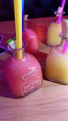 three different colored drinks in small vases on a wooden table with colorful straws