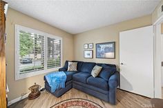 a living room with a blue couch and wooden floors in front of two windows that look out onto the street