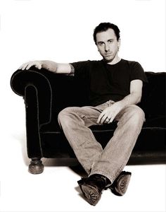 a black and white photo of a man sitting on a couch with his legs crossed