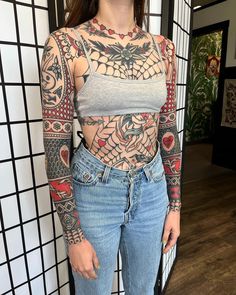 a woman standing in front of a wall with tattoos on her chest and arms,