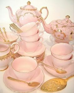 a pink tea set with gold trimmings and matching cups, saucers, and spoons