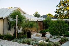 a house that is next to some trees and plants in front of it, with rocks on the ground