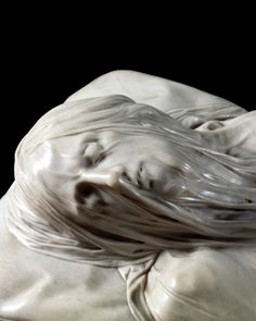 a close up of a white marble statue with flowing hair on it's head