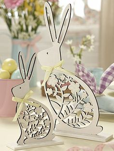 two paper rabbits sitting on top of a table next to some flowers and easter eggs