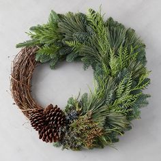 a wreath with pine cones and greenery on it, sitting on a white surface