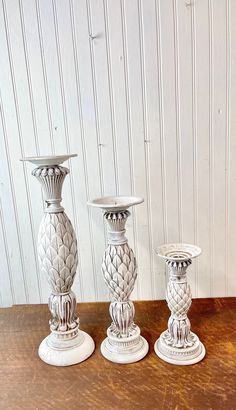 three white vases sitting on top of a wooden table next to eachother