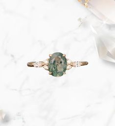 an oval cut green stone ring with three diamonds on the side, sitting on a marble surface