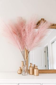 some pink feathers are in a vase on a white mantle with gold accents and a mirror