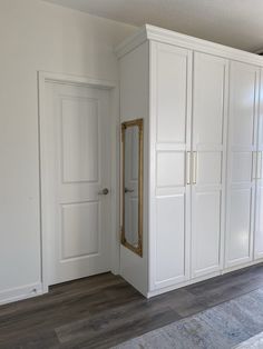 an empty room with white cabinets and wood flooring in front of the door to another room