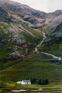 a white house in the middle of a green mountain range with a path leading to it