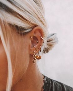 a woman with blonde hair wearing gold earrings and a black shirt is looking down at her ear