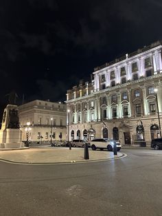 a car is parked in front of a large building at night with its lights on