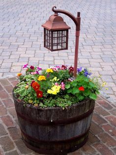 a wooden barrel filled with flowers and a light on top of it next to a brick walkway