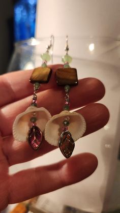 "These beautiful Shell Dangles turn out so gorgeous. I love the colors on the beads & the earthy iridescent brown square Abalone shell on the top section was enhanced with light greens and little hits of hot pink shimmer. These shell dangles have many points of interest.  The Shell Dangle at the bottom has a dark iridescent finish and compliments the light green crystals. The facets catch the light and sparkle from top to bottom.  All of my designs are original so you won't see any other person wearing anything like this.  I hand pick items from nature to incorporate in hand created \"ONE OF A KIND\" items! I found these SHELLS on the shorelines of the Oregon/California boarder.  SHELLS are gentle healers and messengers, and very powerful tools of transformation.  With all natural stones a Light Green Crystals, Dark Iridescent, Ocean Shells, Brown Square, Nature Earrings, Be Natural, Beach Vibes, Abalone Shell, Beach Vibe