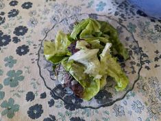 a glass bowl filled with lettuce on top of a floral tablecloth covered table