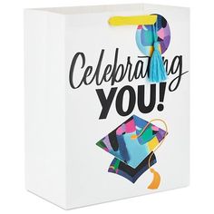 a white gift bag with the words celebrating you printed on it and a graduation cap