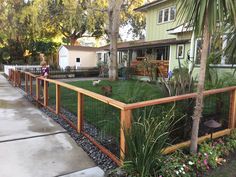 a fenced in area with plants and flowers on the side walk next to a house