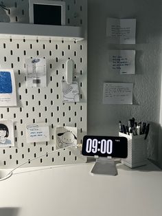 an office desk with a clock on it and several notes attached to the wall behind it