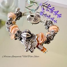 This exquisite Bohemian style glass bead Butterfly Charm bracelet is crafted with 12mm Artisan Lampwork glass bicone beads in a stunning peachy/orange base encased in clear glass by glass artist Lynda Cogbill, each adorned with Karen Hill Tribes Silver bead caps. Featuring a 12mm ornate Karen Hill Tribe Silver focal bead at the center, oxidized to reveal intricate pattern detail, accompanied by a Karen Hill Tribe Silver Butterfly Charm and tiny orange Sapphire Charm symbolizing change, growth, h Apricot Beaded Round Bead Jewelry, Hand-strung Silver Czech Glass Jewelry, Handmade Peach Bracelets With Round Beads, Handmade Peach Beaded Bracelets As Gift, Handmade Peach Beaded Bracelets For Gift, Handmade Peach Bracelet Gift, Adjustable Peach Bracelet, Bohemian Nickel-free Charm Bracelet With Round Beads, Artisan Beaded Bracelets With Nickel-free Round Beads