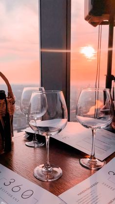 two wine glasses sitting on top of a wooden table next to a basket and menu