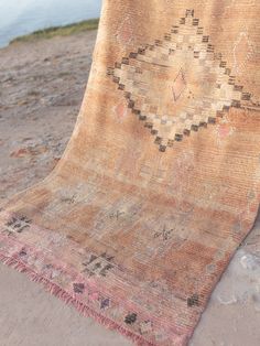 an old rug is laying on the sand by the water's edge, with a boat in the background