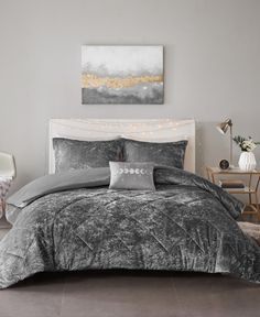 a bed with grey and white comforter in a bedroom next to a painting on the wall