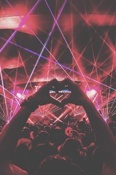 a person making a heart shape with their hands at a music festival in the dark