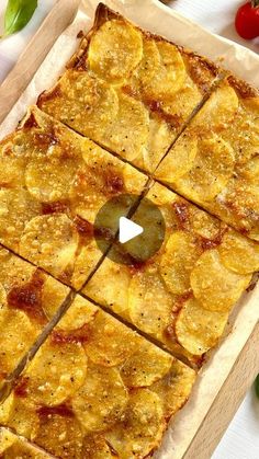 a pizza cut into squares on top of a cutting board next to tomatoes and peppers