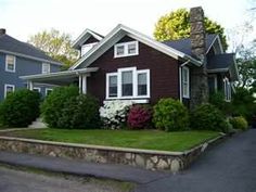 a brown house with white trim and flowers in the front yard on a sunny day