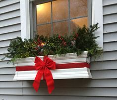 a red bow is tied on the window sill with evergreens and berries in it