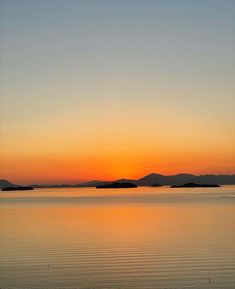 the sun is setting over water with mountains in the distance