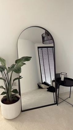 a mirror sitting on top of a white floor next to a table with a potted plant