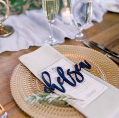 a place setting with wine glasses, napkins and utensils on a wooden table