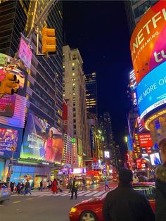 a busy city street at night with people crossing the street and billboards lit up