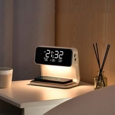 an alarm clock sitting on top of a white table next to a cup and candle