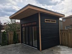 a small black building sitting on top of a stone patio next to a wooden fence