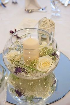 there is a glass bowl with flowers and candles in it on top of the table