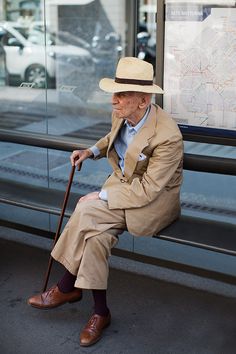 an old man in a suit and hat sitting on a bench with his cane up