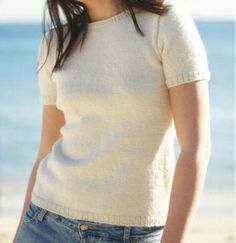 a woman standing on top of a sandy beach next to the ocean with her hands in her pockets